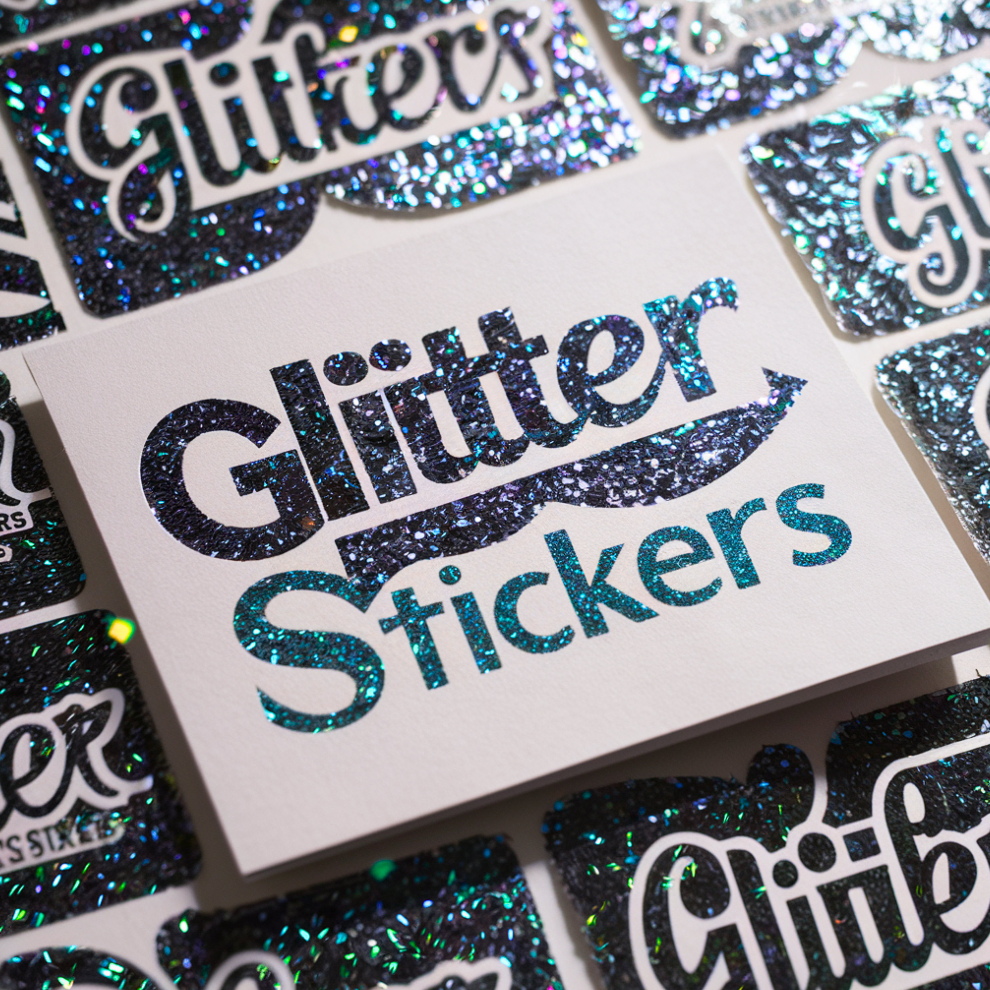 This image focuses on a collection of glitter stickers arranged on a flat surface. The stickers feature the word "Glitter" prominently in sparkly, holographic letters, emphasizing the glittery texture of the design. The background of the stickers is white, which enhances the contrast and makes the glitter effect more pronounced.