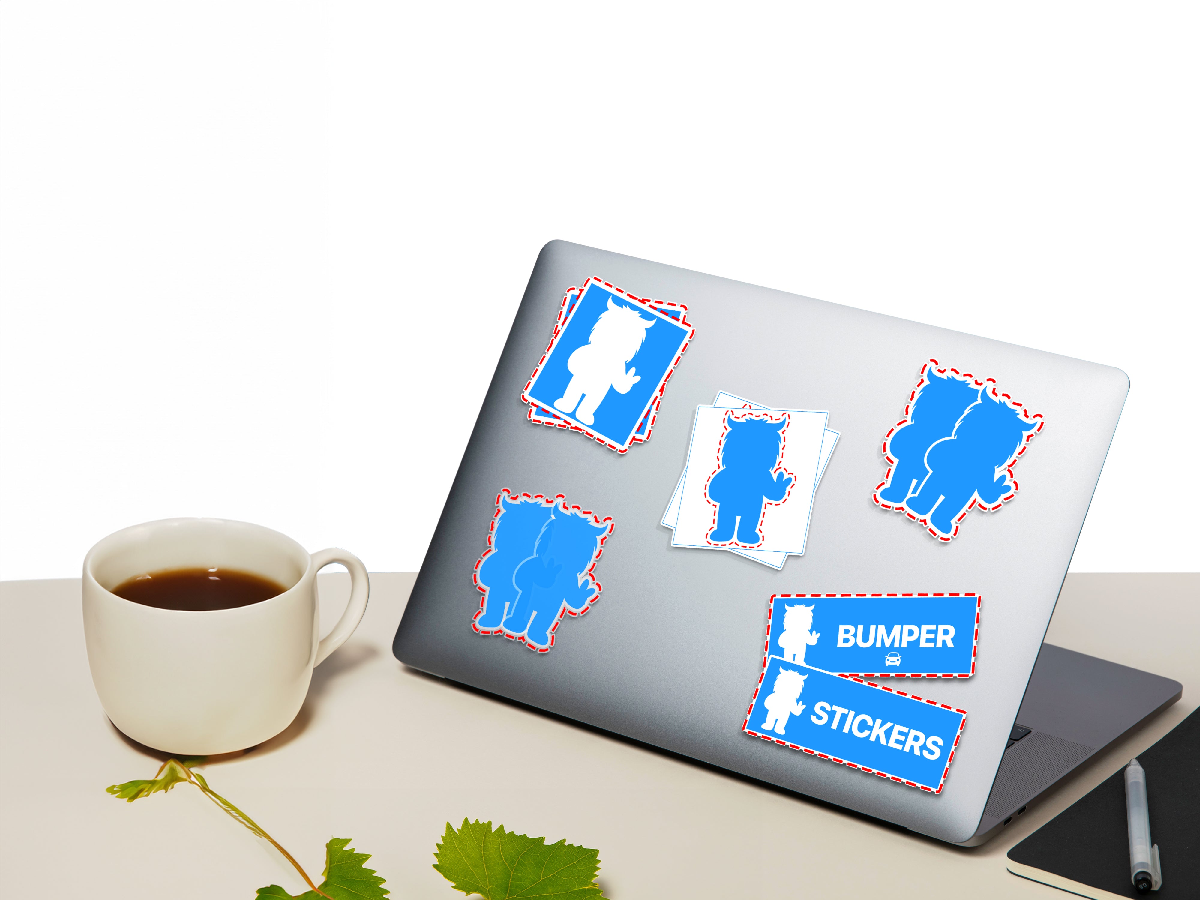 This image displays a laptop with various blue and white stickers attached to its surface. The stickers feature cartoonish silhouettes outlined with a dashed red border. The laptop is placed on a clean desk alongside a cup of tea and a pen, with a green leaf resting on the desk as well. The background is plain white, allowing the stickers to stand out clearly on the laptop.